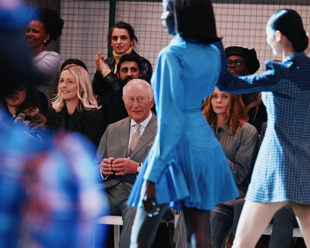 King Charles III watches from the front row as models walk the runway in blue looks during Tolu Coker at London Fashion Week (February 2026).